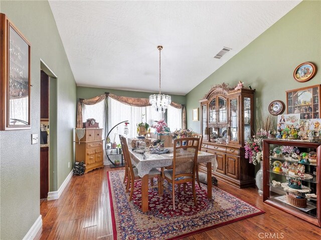 dining room with lofted ceiling, a notable chandelier, wood-type flooring, and a textured ceiling