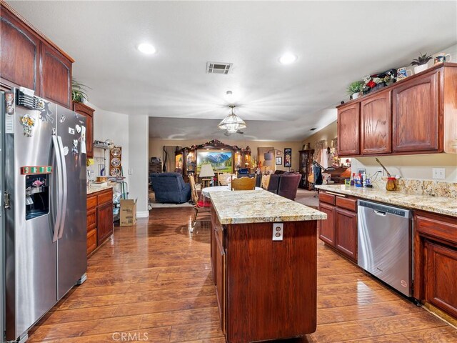 kitchen featuring dark wood-type flooring, appliances with stainless steel finishes, a center island, light stone countertops, and decorative light fixtures