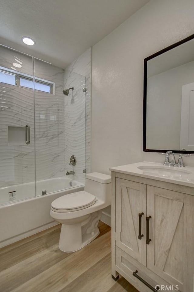 full bathroom featuring vanity, hardwood / wood-style flooring, bath / shower combo with glass door, and toilet