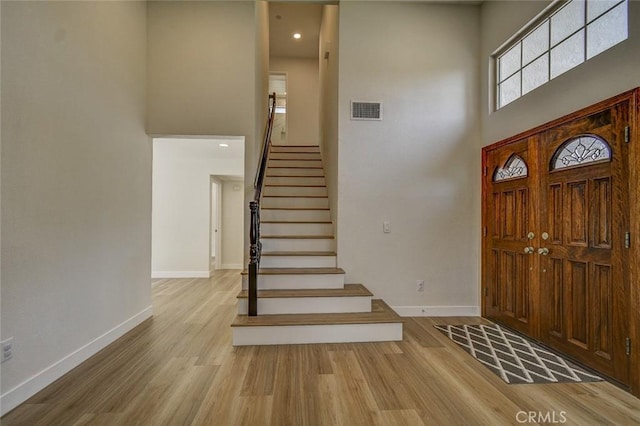 foyer entrance featuring a towering ceiling and light wood-type flooring