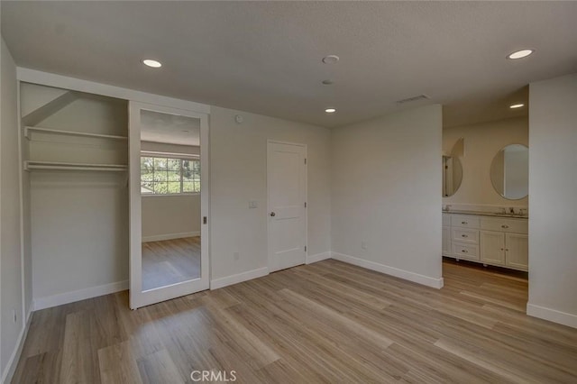 unfurnished bedroom featuring a closet, sink, light hardwood / wood-style floors, and ensuite bath