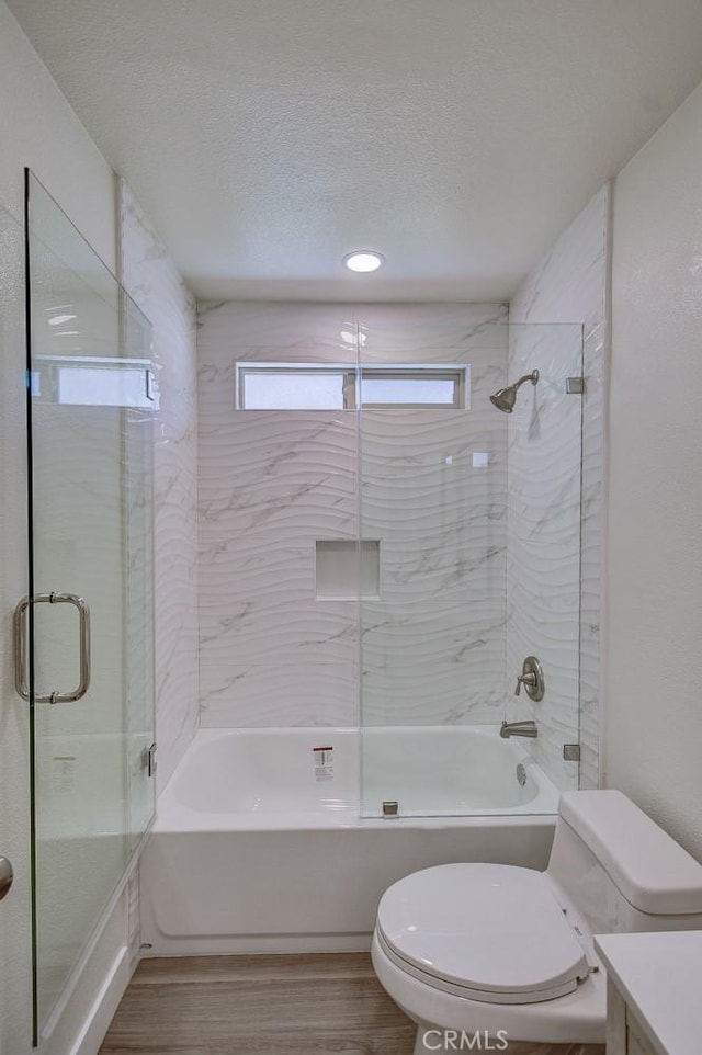 full bathroom featuring hardwood / wood-style floors, bath / shower combo with glass door, vanity, a textured ceiling, and toilet