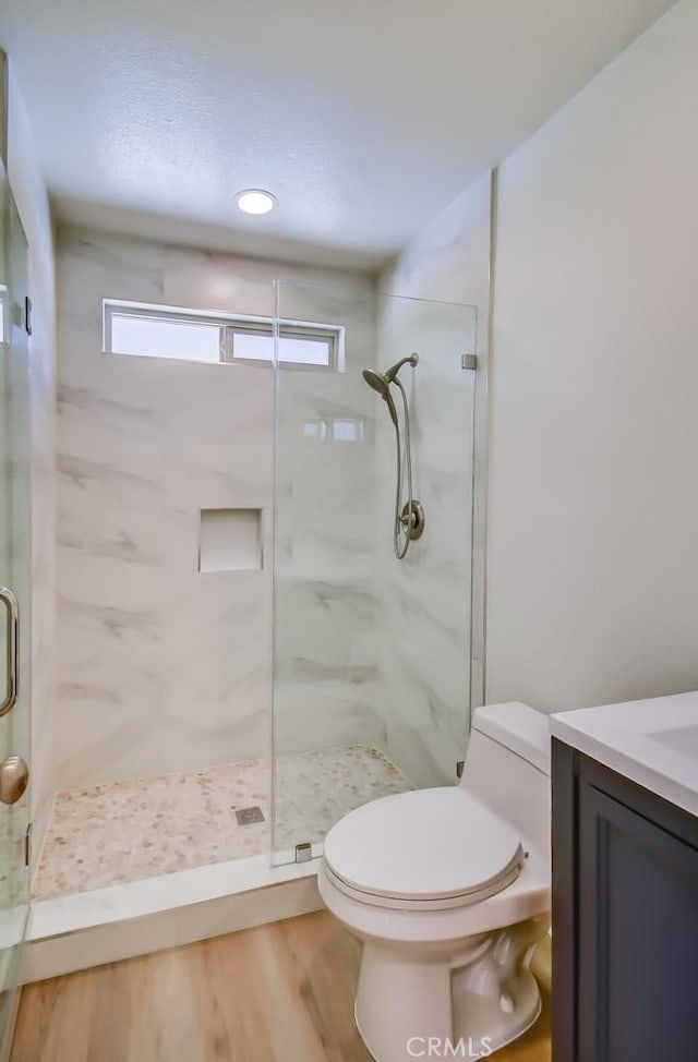 bathroom with a shower with door, vanity, hardwood / wood-style floors, and toilet