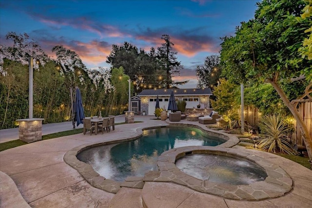 pool at dusk featuring a patio area, an outdoor structure, and an in ground hot tub