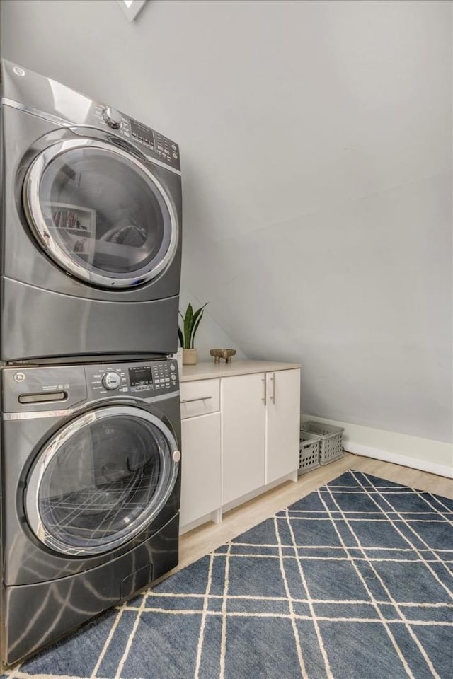 clothes washing area featuring cabinets, stacked washing maching and dryer, and light hardwood / wood-style flooring