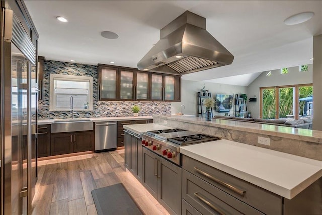 kitchen featuring sink, appliances with stainless steel finishes, hardwood / wood-style floors, island exhaust hood, and decorative backsplash