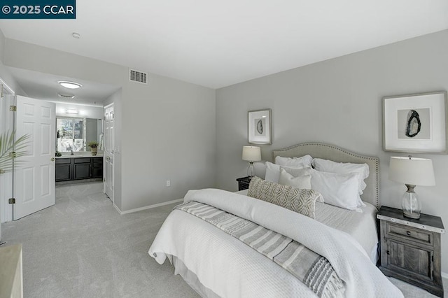 bedroom with ensuite bathroom and light carpet