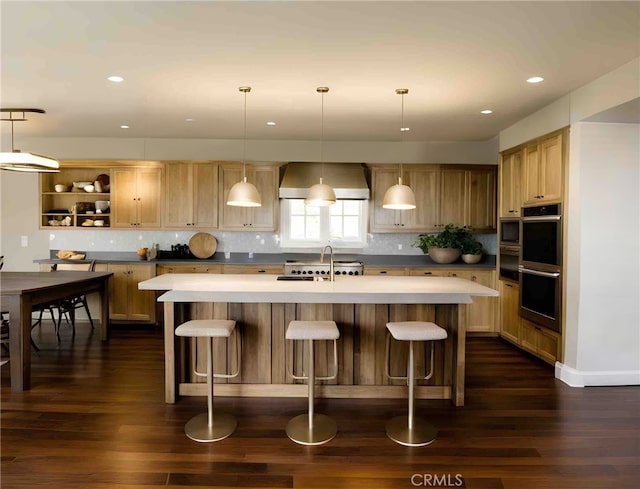 kitchen featuring hanging light fixtures, a kitchen island with sink, dark wood-type flooring, and wall chimney exhaust hood