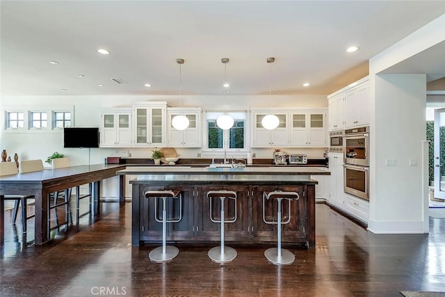 kitchen featuring a breakfast bar area, stainless steel appliances, an island with sink, white cabinets, and decorative light fixtures