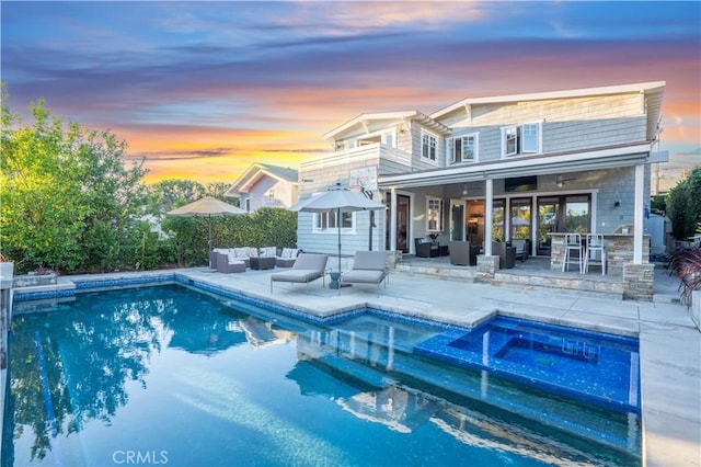 back house at dusk with an outdoor living space, a swimming pool with hot tub, and a patio area