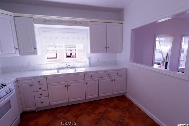 kitchen with sink, white cabinets, dark tile patterned floors, tile counters, and gas range gas stove