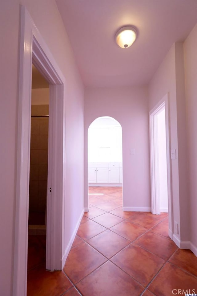 hall featuring arched walkways, light tile patterned floors, and baseboards