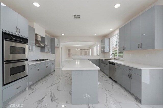 kitchen with gray cabinetry, stainless steel appliances, a center island, and wall chimney exhaust hood