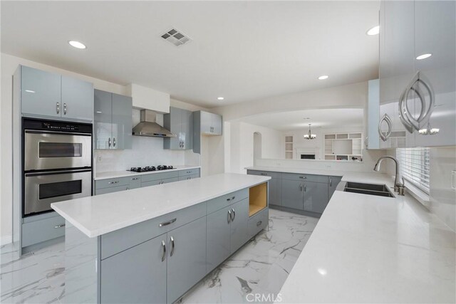 kitchen featuring sink, gray cabinets, wall chimney exhaust hood, black gas stovetop, and stainless steel double oven