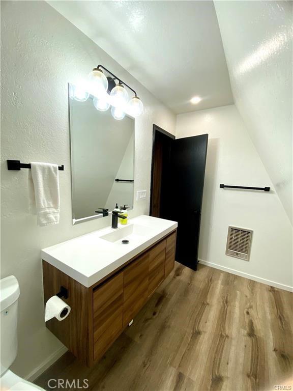 bathroom with wood-type flooring, vaulted ceiling, vanity, and toilet