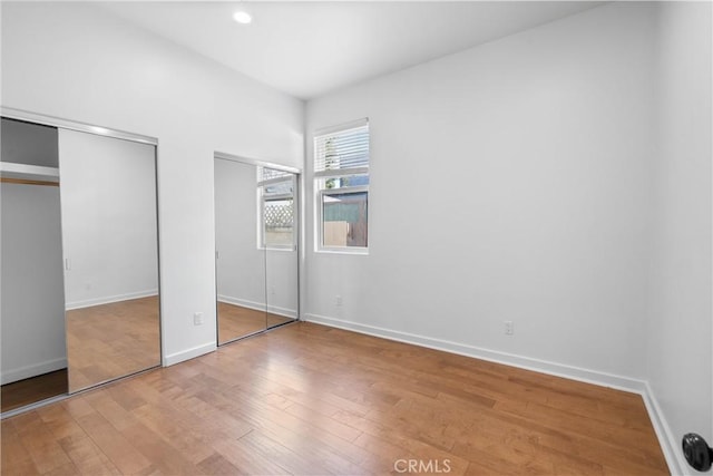 unfurnished bedroom featuring light hardwood / wood-style floors and two closets