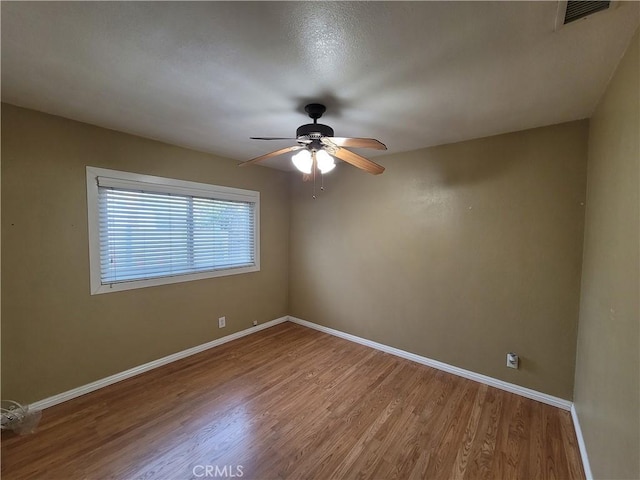 unfurnished room featuring ceiling fan, wood finished floors, visible vents, and baseboards