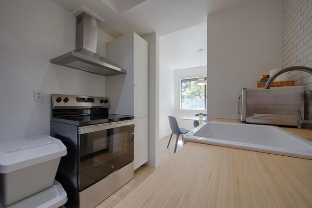 kitchen with wall chimney exhaust hood, stainless steel range with electric cooktop, and light hardwood / wood-style flooring