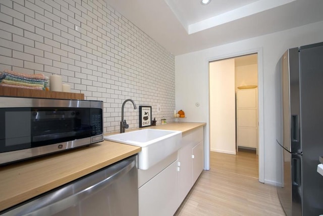 kitchen with sink, white cabinetry, light hardwood / wood-style flooring, stainless steel appliances, and backsplash