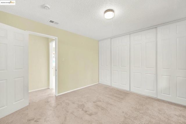 unfurnished bedroom featuring light carpet, a closet, and a textured ceiling