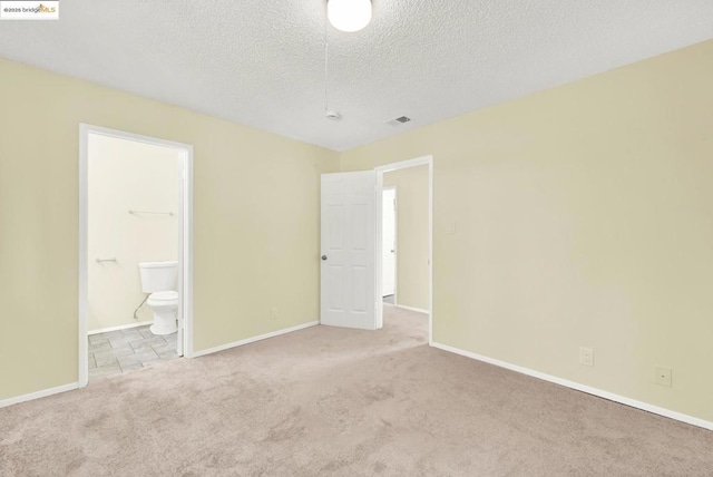 unfurnished bedroom with connected bathroom, light carpet, and a textured ceiling