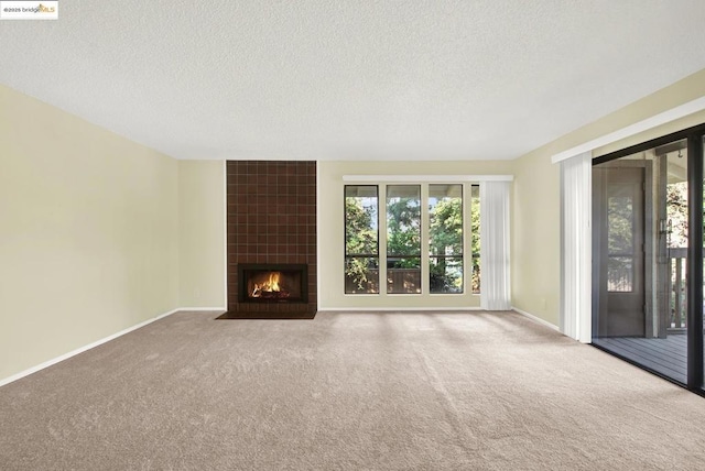 unfurnished living room with a tiled fireplace, carpet floors, and a textured ceiling