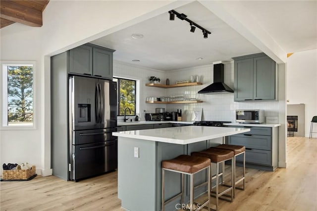 kitchen with light hardwood / wood-style flooring, a breakfast bar, tasteful backsplash, black refrigerator with ice dispenser, and wall chimney exhaust hood