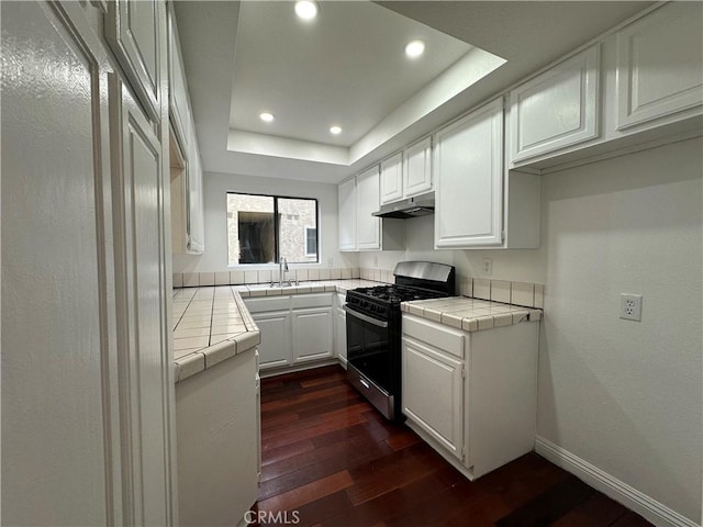 kitchen featuring stainless steel range with gas cooktop, white cabinets, tile counters, a tray ceiling, and dark wood-type flooring