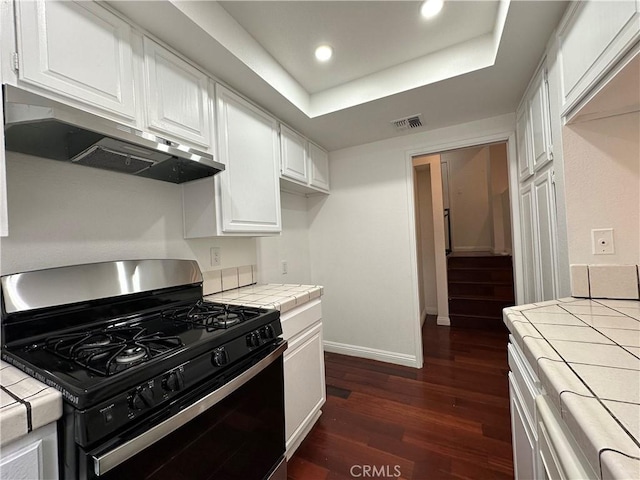 kitchen featuring a raised ceiling, tile counters, white cabinets, and black gas range