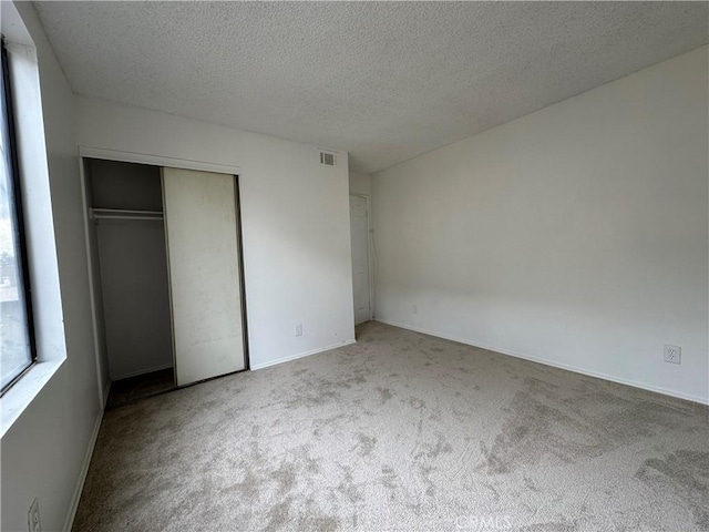 unfurnished bedroom with light colored carpet, a textured ceiling, and a closet