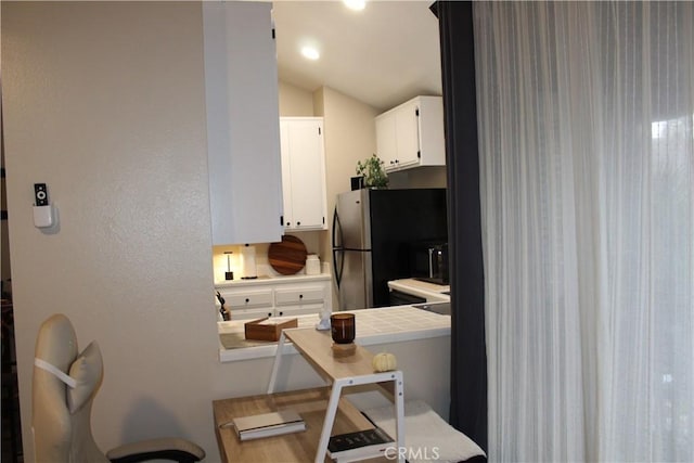 kitchen with vaulted ceiling, tile counters, fridge with ice dispenser, and white cabinets