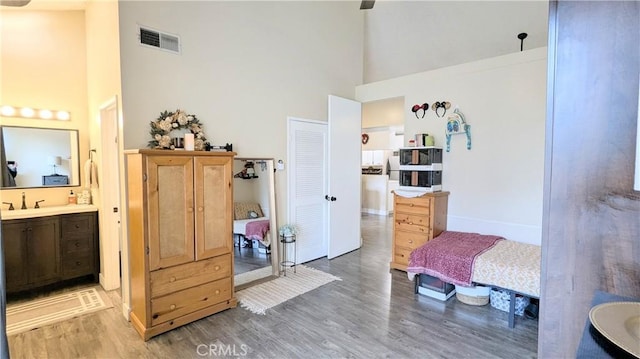 bedroom with connected bathroom, hardwood / wood-style floors, sink, and a high ceiling