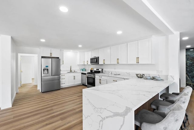 kitchen with stainless steel appliances, light hardwood / wood-style flooring, white cabinets, and kitchen peninsula