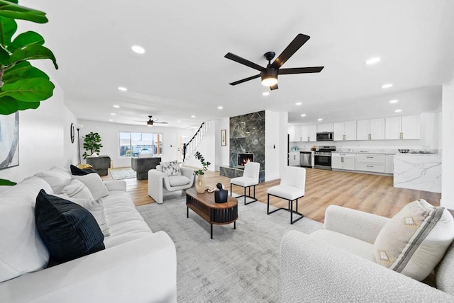 living room featuring a high end fireplace, light hardwood / wood-style flooring, and ceiling fan