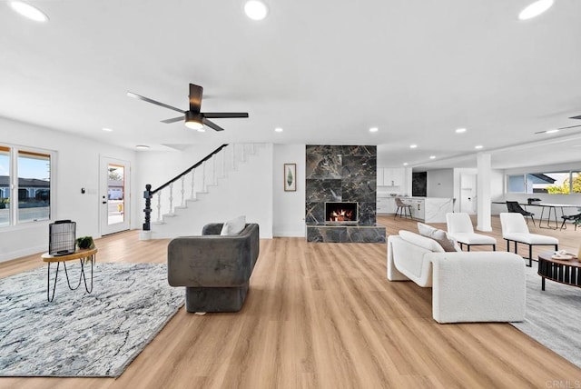 living room featuring plenty of natural light, light hardwood / wood-style floors, a premium fireplace, and ceiling fan