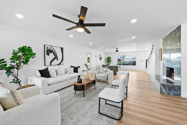 living room with ceiling fan, a premium fireplace, and light hardwood / wood-style flooring