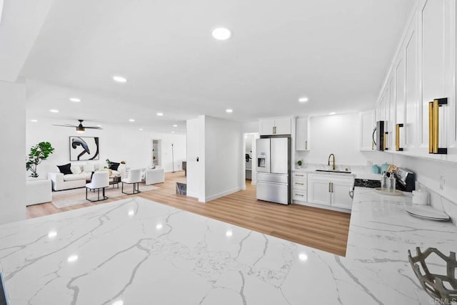 kitchen featuring sink, white cabinetry, light wood-type flooring, stainless steel appliances, and light stone countertops