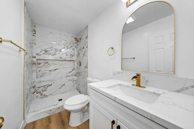 bathroom featuring hardwood / wood-style flooring, vanity, tiled shower, and toilet