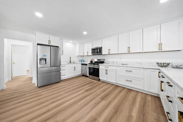 kitchen with stainless steel appliances, light stone countertops, sink, and white cabinets