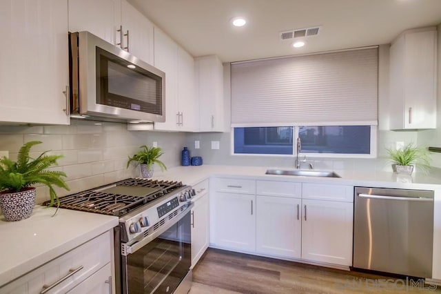 kitchen featuring sink, appliances with stainless steel finishes, white cabinetry, backsplash, and light hardwood / wood-style floors