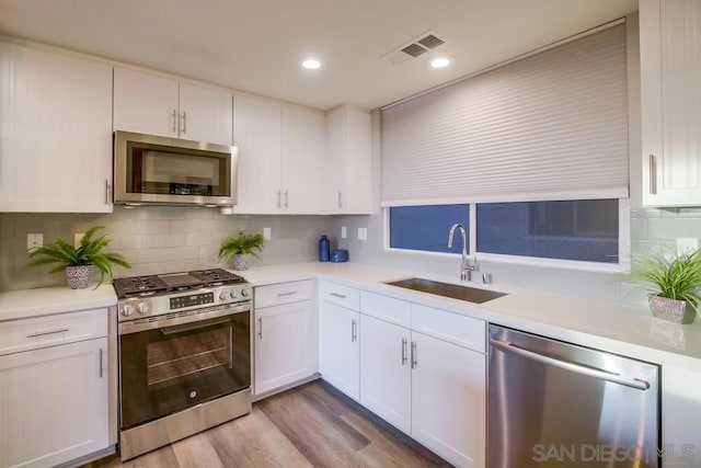 kitchen with white cabinetry, sink, decorative backsplash, stainless steel appliances, and light hardwood / wood-style flooring