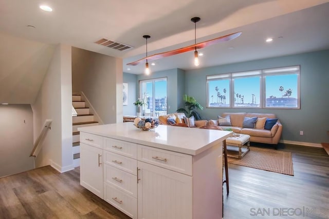 kitchen featuring hanging light fixtures, white cabinetry, wood-type flooring, and a kitchen bar