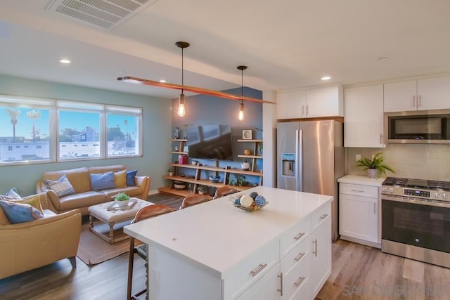 kitchen with pendant lighting, white cabinetry, stainless steel appliances, wood-type flooring, and a kitchen island