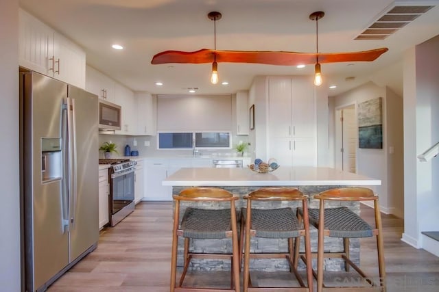 kitchen featuring sink, light hardwood / wood-style flooring, appliances with stainless steel finishes, white cabinetry, and decorative light fixtures