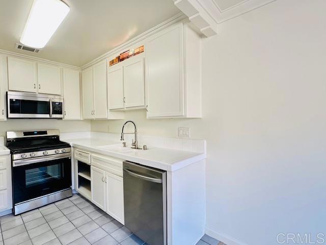 kitchen featuring sink, light tile patterned floors, stainless steel appliances, and white cabinets