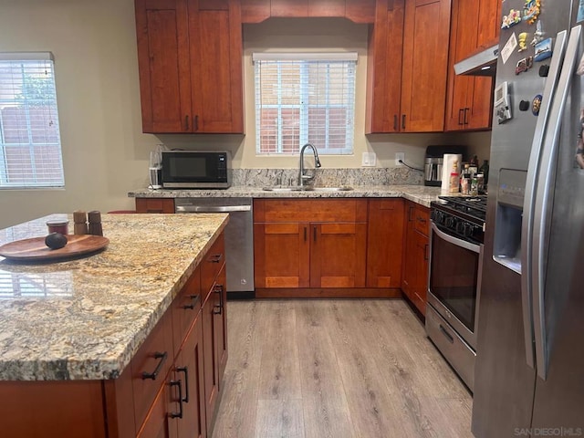 kitchen with sink, light hardwood / wood-style flooring, appliances with stainless steel finishes, light stone countertops, and a healthy amount of sunlight