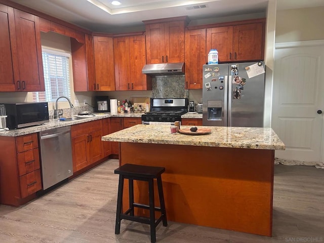 kitchen featuring light stone counters, stainless steel appliances, sink, and a kitchen island