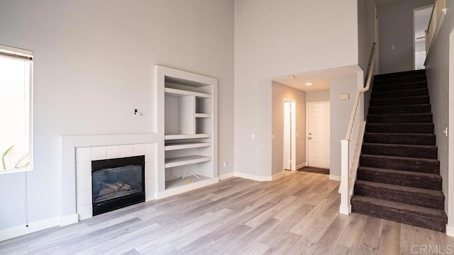 unfurnished living room featuring built in shelves, a fireplace, a high ceiling, and light wood-type flooring