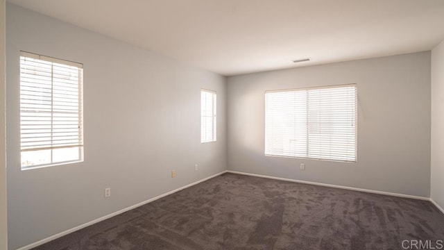 unfurnished room with dark carpet and a wealth of natural light