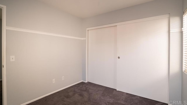 unfurnished bedroom with dark colored carpet and a closet